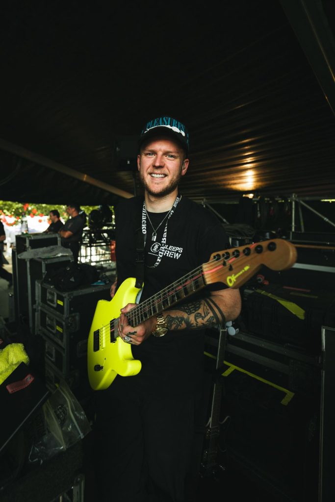A photo of Miles smiling, holding a yellow guitar backstage